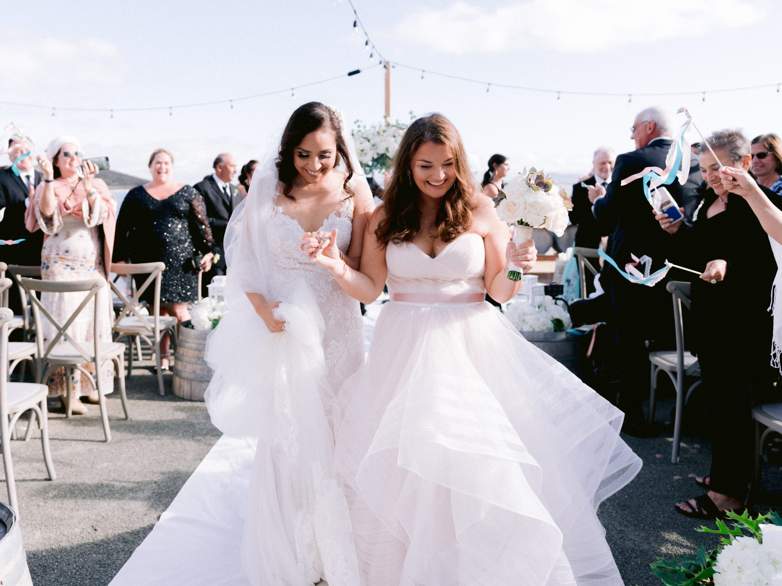 Small Wedding Trend: Bride and bride holding hands after ceremony with small micro wedding cheering them on the background, outside in the San Francisco Bay Area