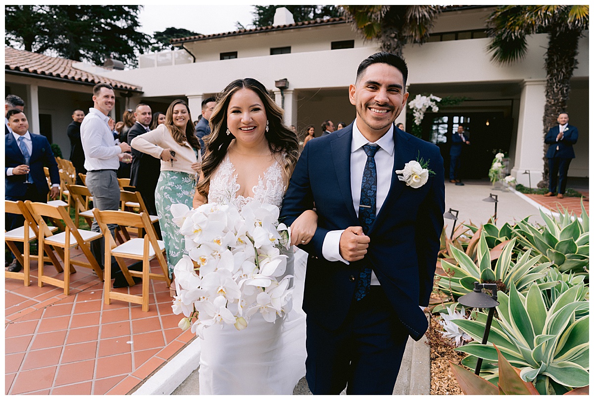 Keyla and Renato, smiling, leaving their wedding ceremony