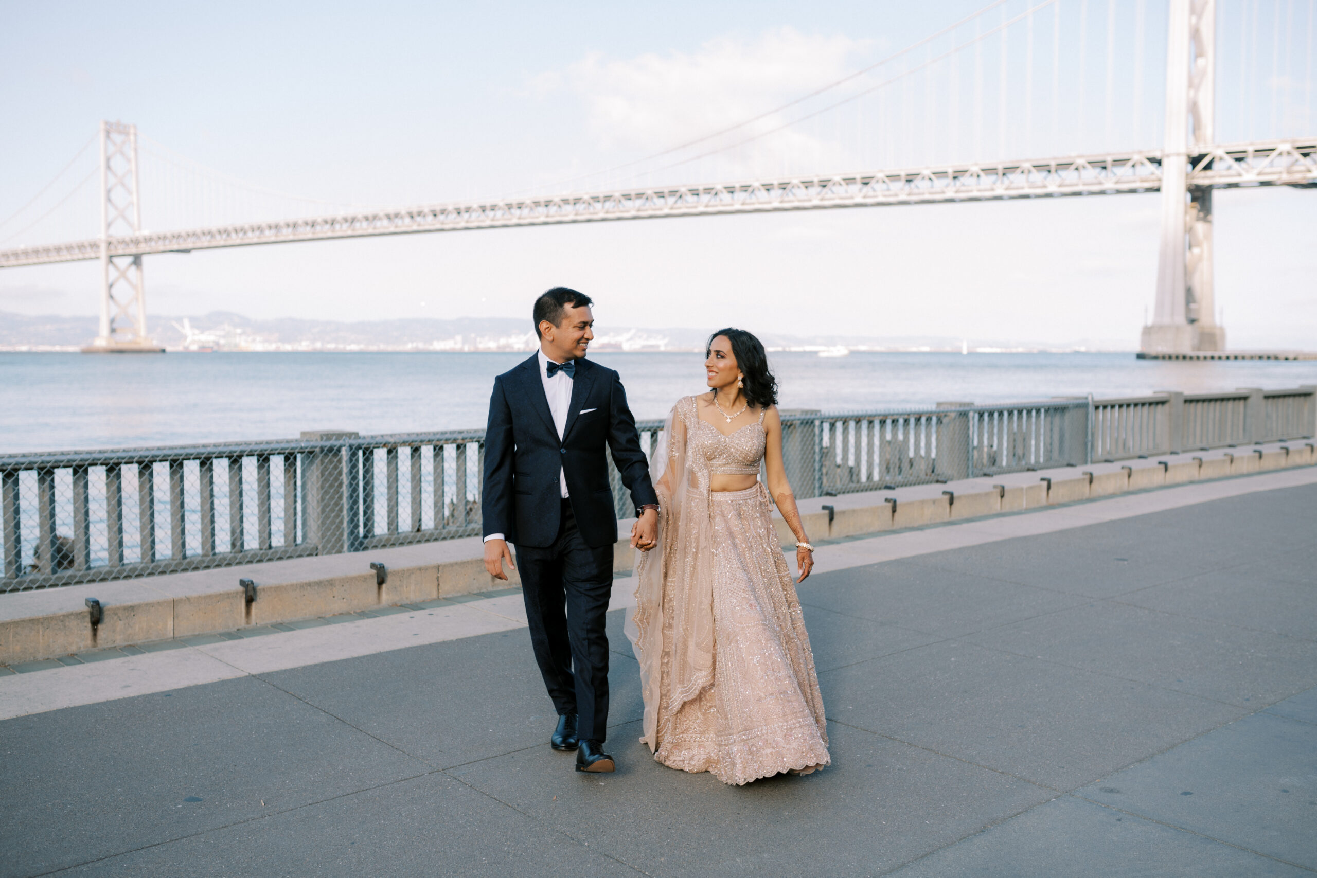 newlywed couple walking with bay bridge backdrop