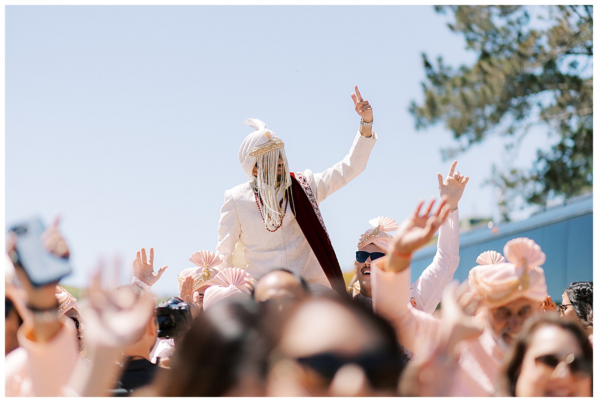 Indian groom on friends shoulders during baraat