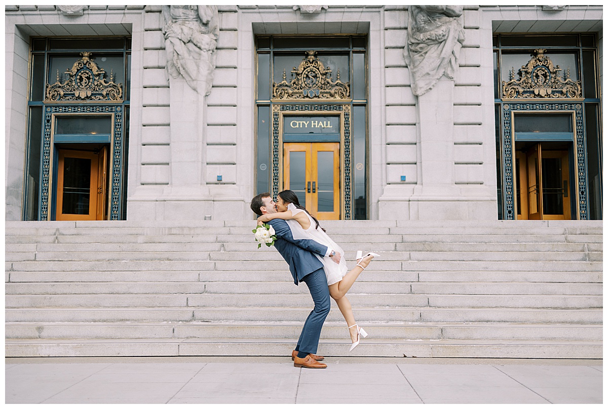 groom lifting up bride for a kiss outside of San Francisco city hall
