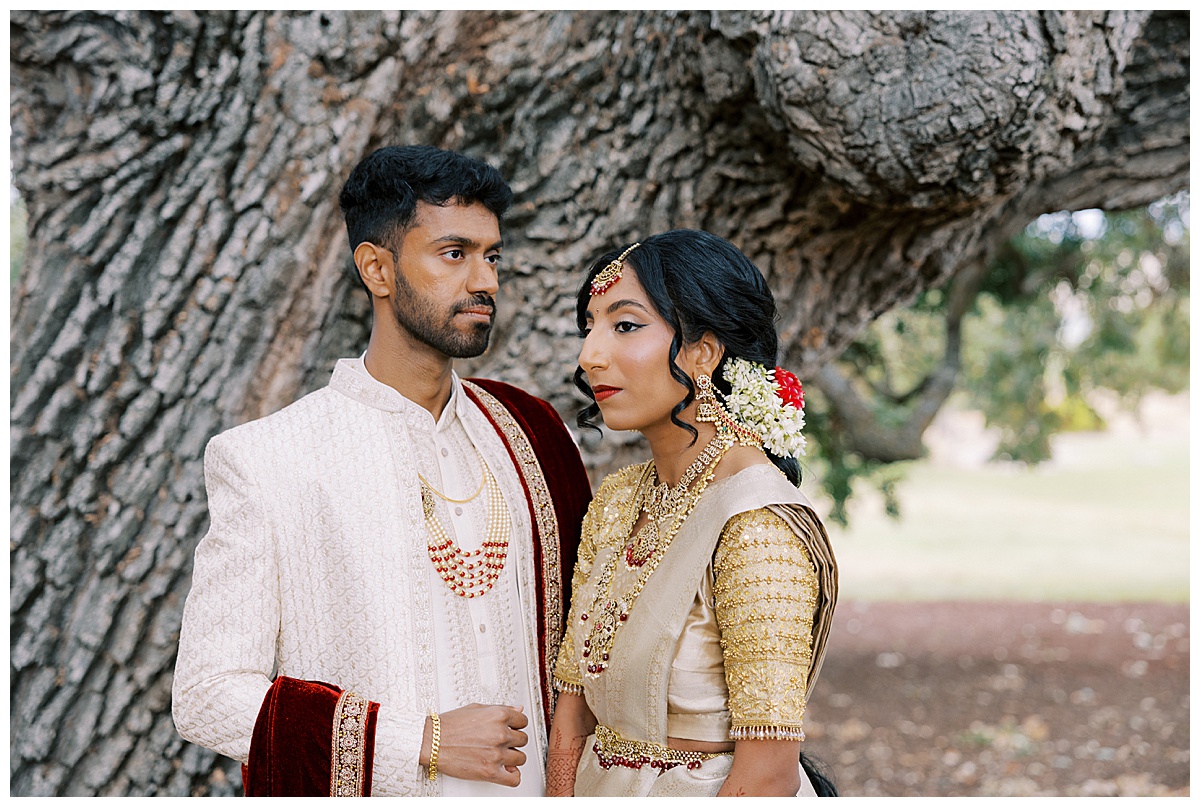 first look at the club at ruby hill. Couple in indian wedding attire standing in front of a tree