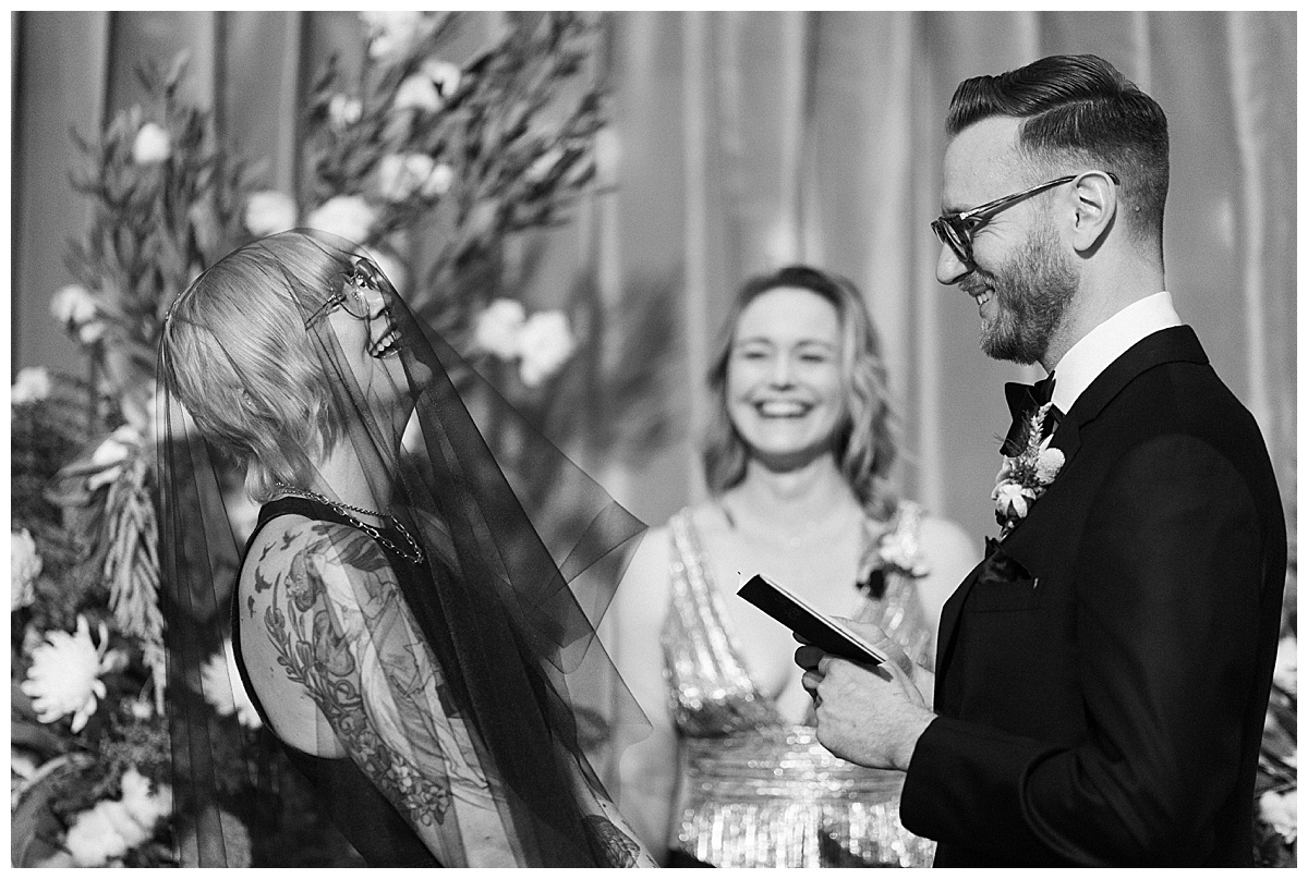 bride throws back head in laughter while groom reads vows