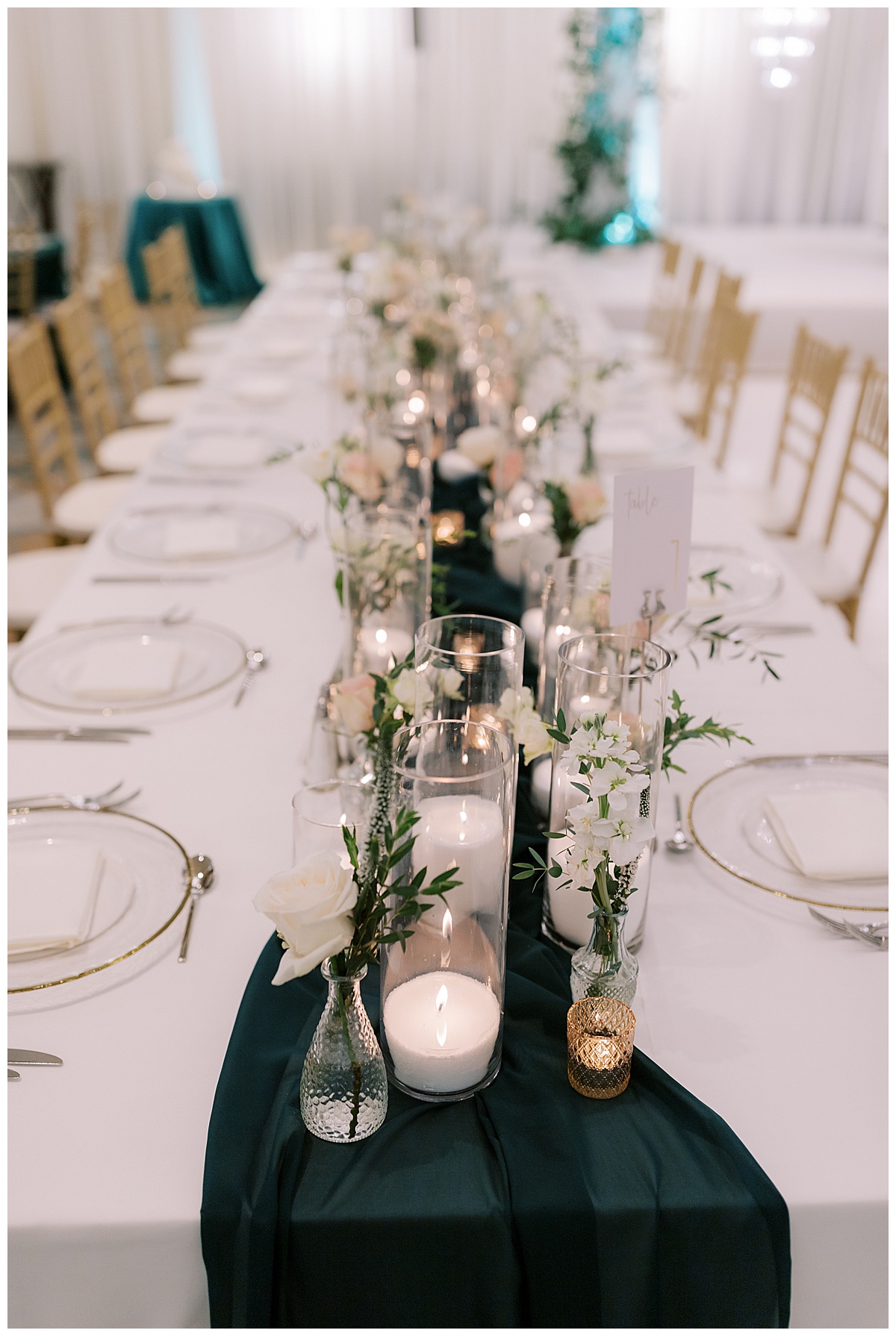 White roses and. hurricane candles in the center of long tables at a Hyatt SFO wedding reception.