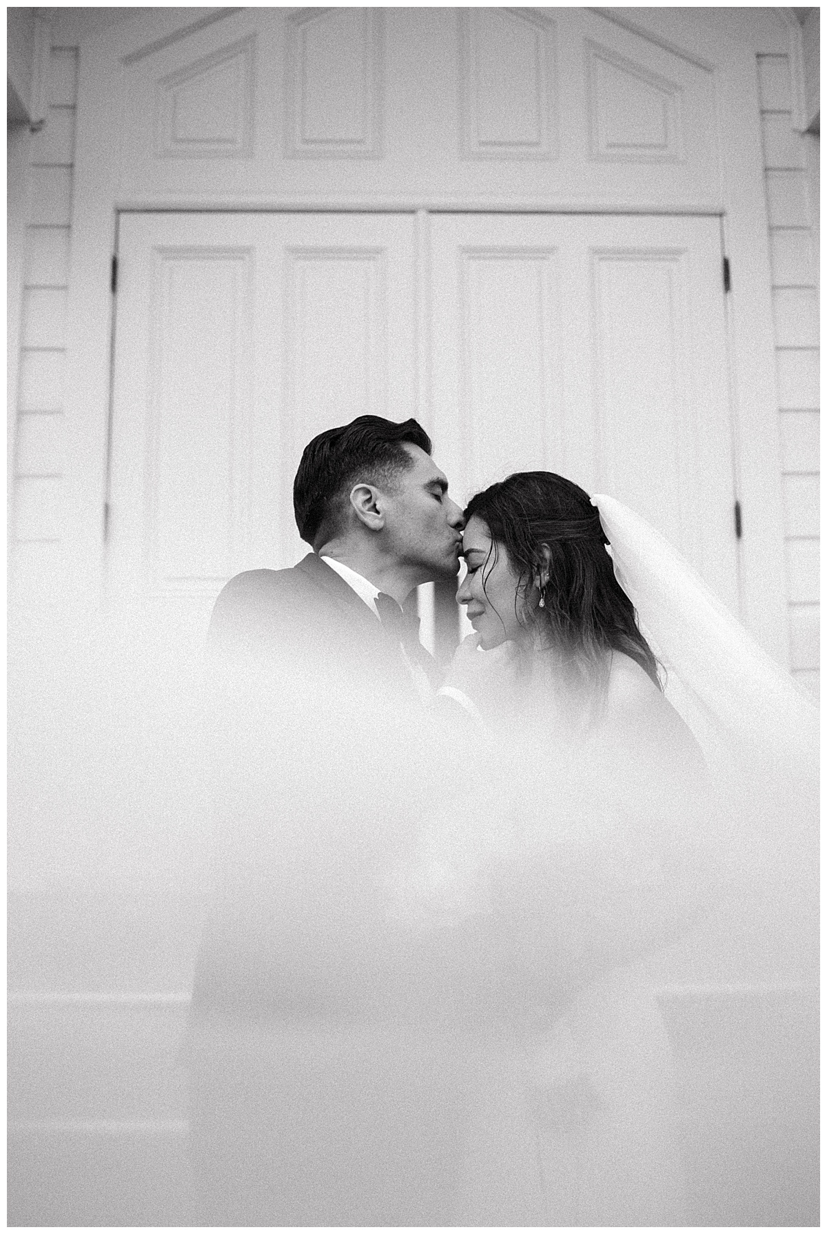 black and white portrait of groom kissing brides forehead