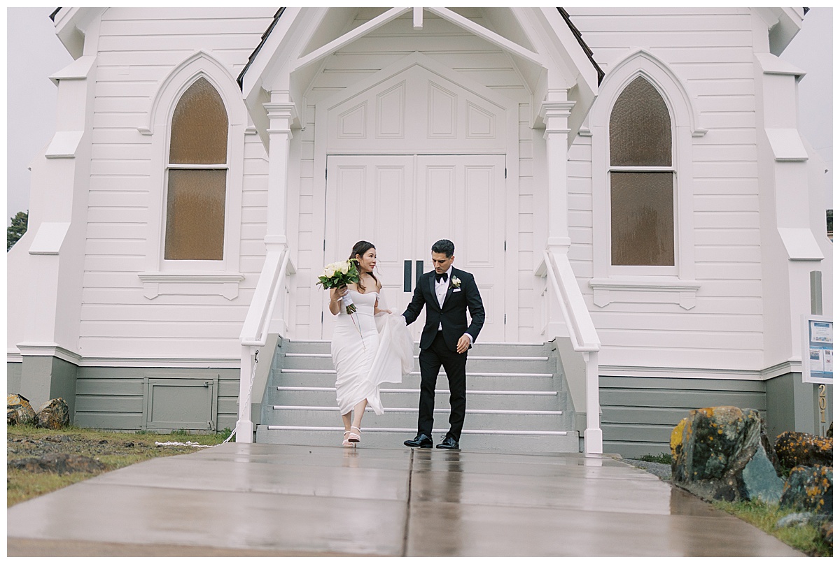 couple walking hand in hand down the steps in front of old st. Hilary's church after their elopement 