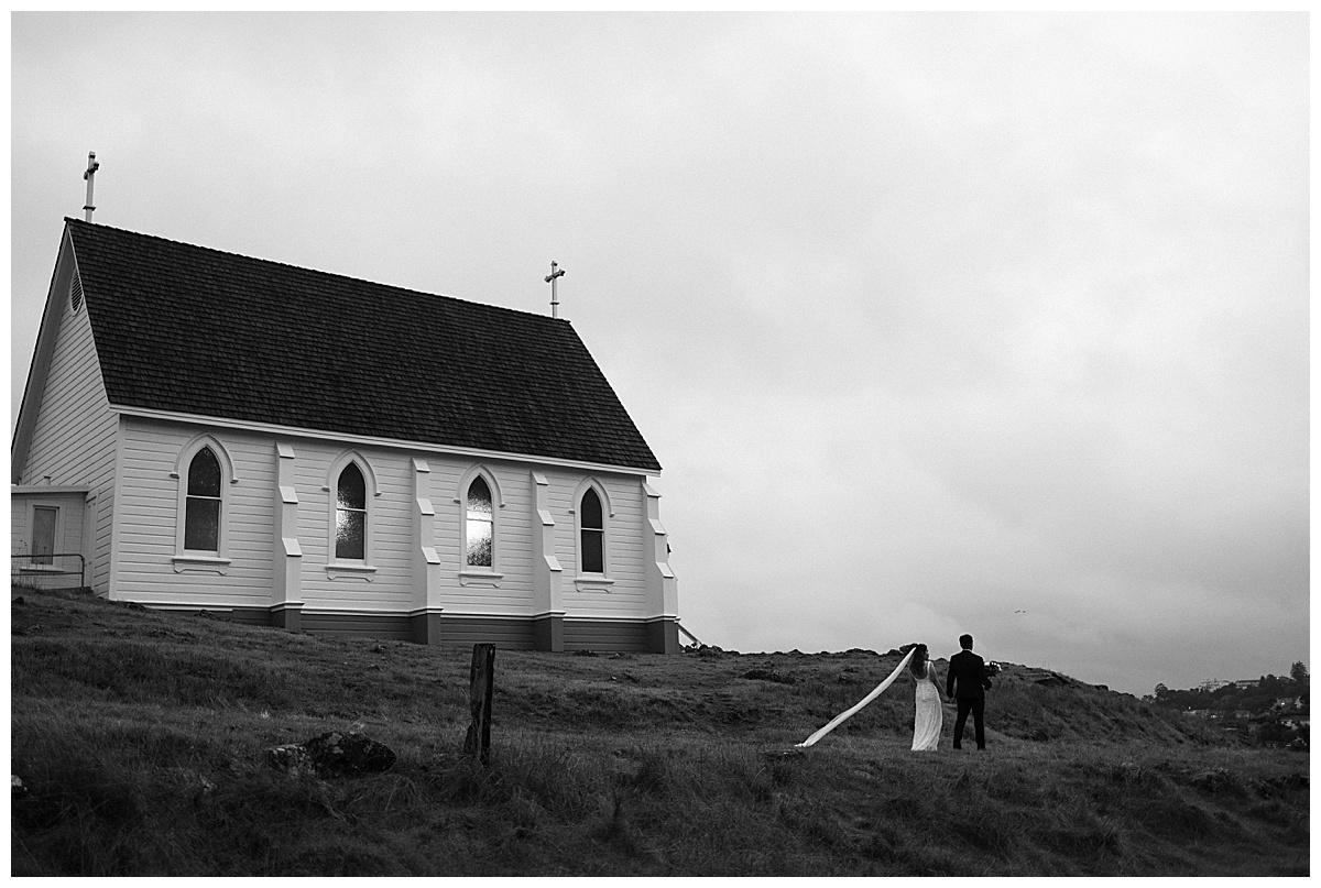wide landscape of couple walking in front of old st Hilarys church in Tiburon