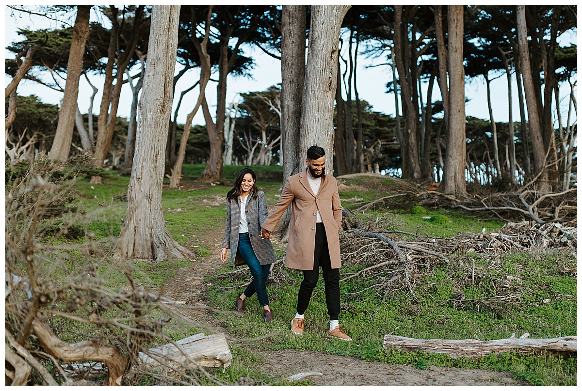 couple walking through trees at sutro baths during engagement session