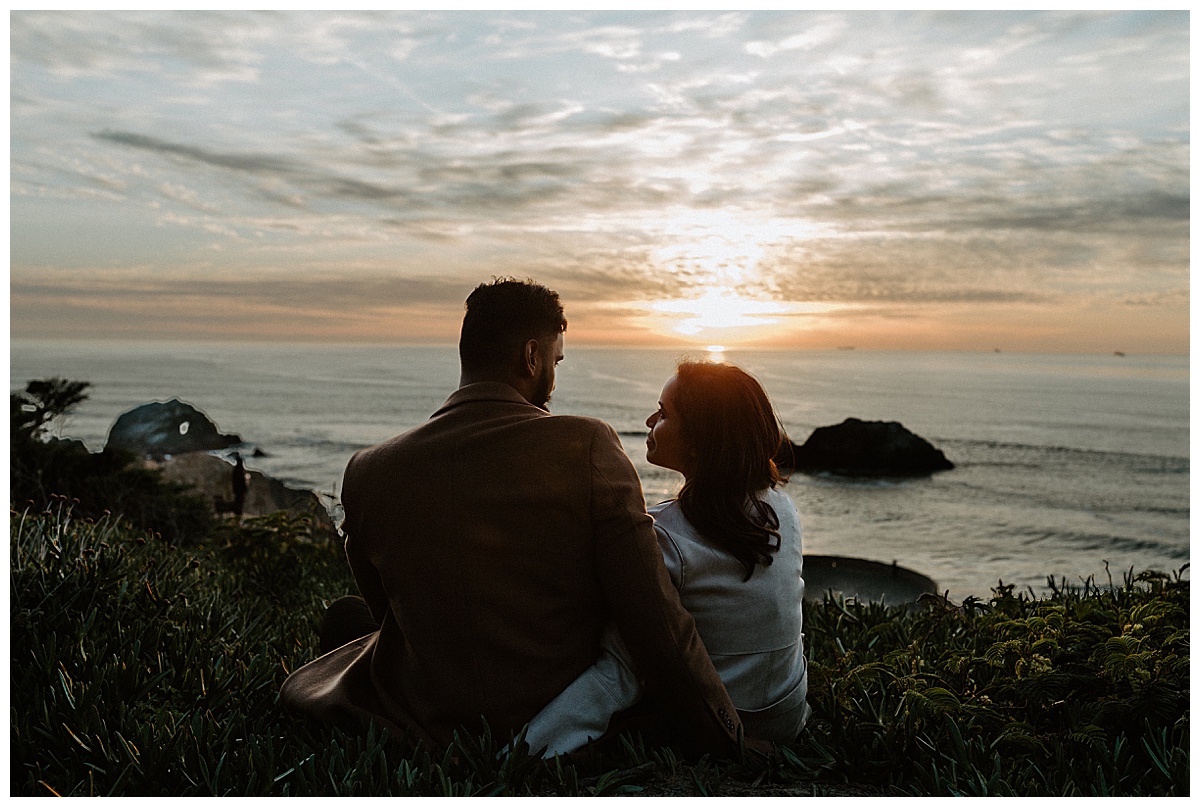 couple sitting at sunset at sutro baths during engagement session