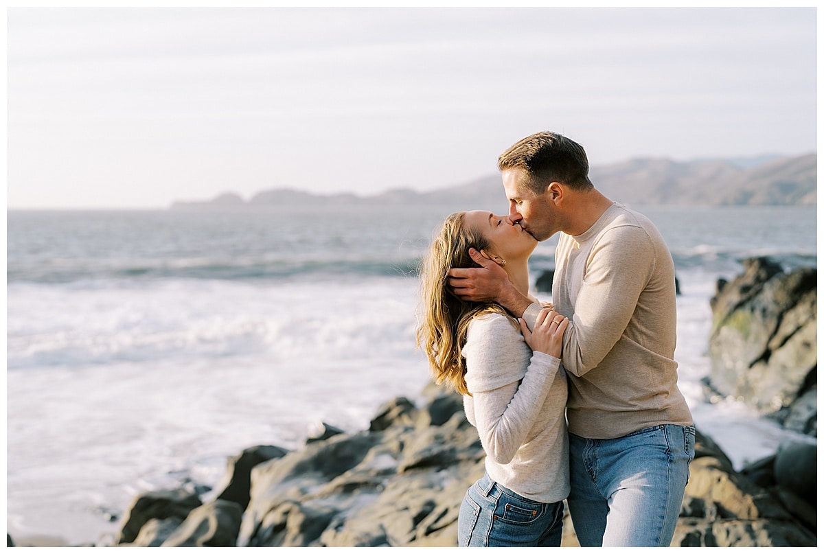 couple kissing on the rocks at baker beach during engagement photos