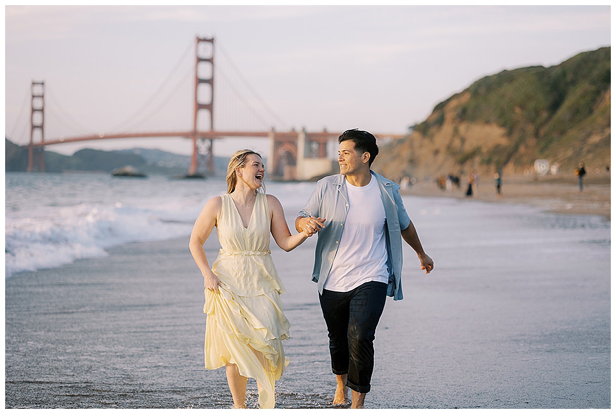 couple running on the beach during engagement session at baker beach